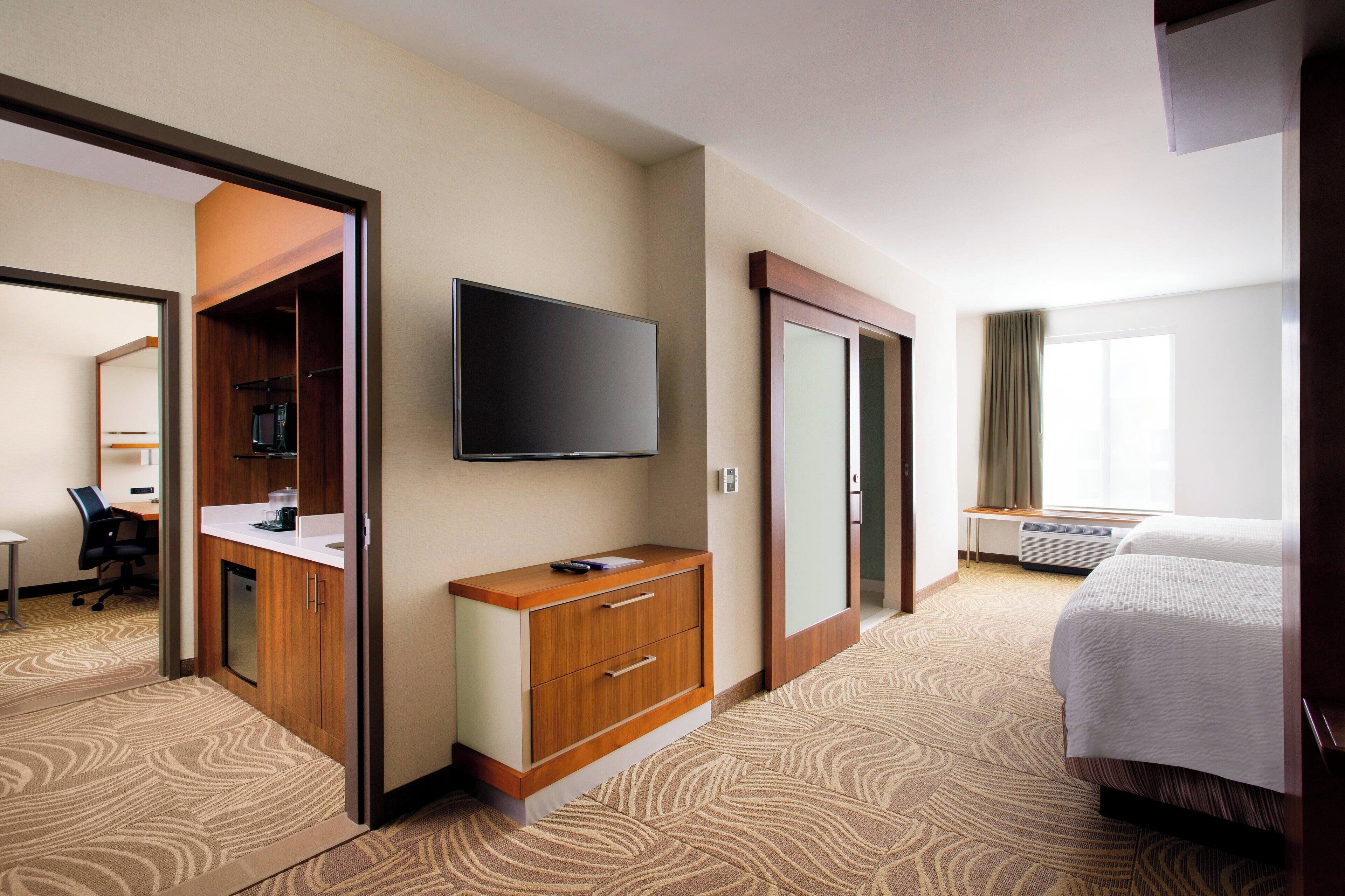 Quarto de hotel com cama, televisão na parede, escrivaninha com cadeira e guarda-roupa.