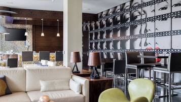 A modern hotel lobby with a sofa, chairs, a dining area, and a large film strip mural on the wall.