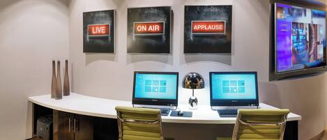 A modern office space with two desks, two chairs, and three illuminated signs reading "LIVE," "ON AIR," and "APPLAUSE."