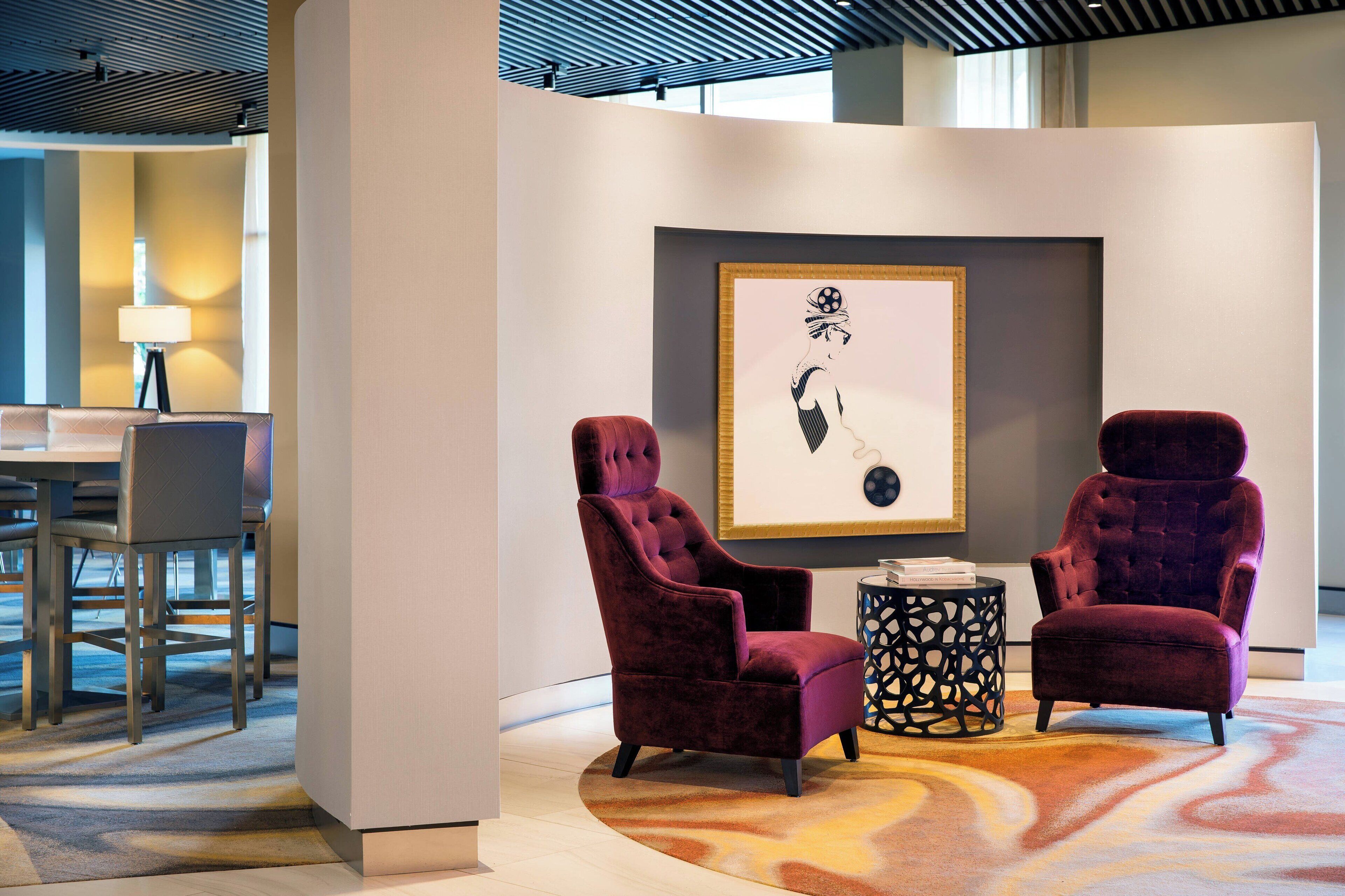 A modern lounge area with two plush armchairs, a round table, and a framed artwork on the wall.