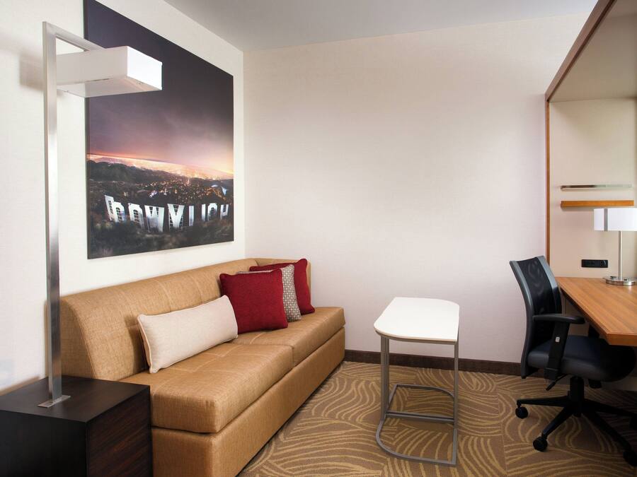 Habitación de hotel con sofá, escritorio, silla, lámpara y un cartel grande en la pared.