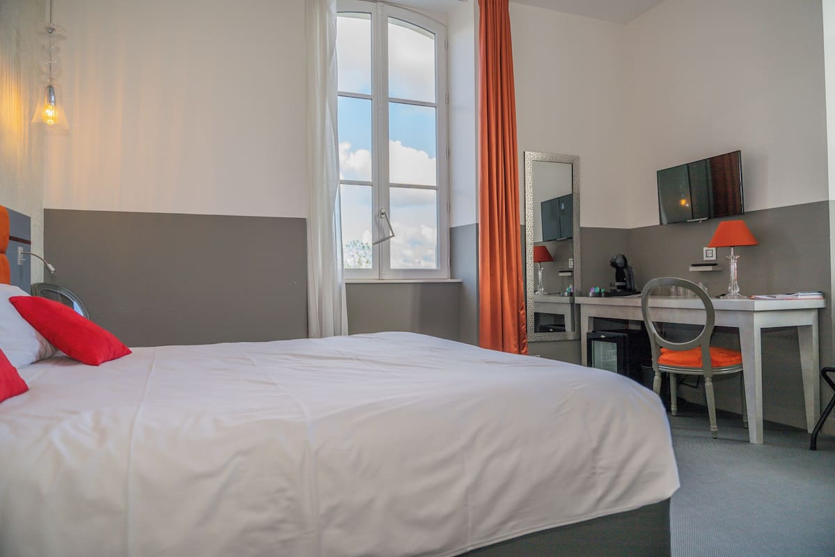 Una habitación de hotel con cama, escritorio, silla, televisor y ventana con cortinas.