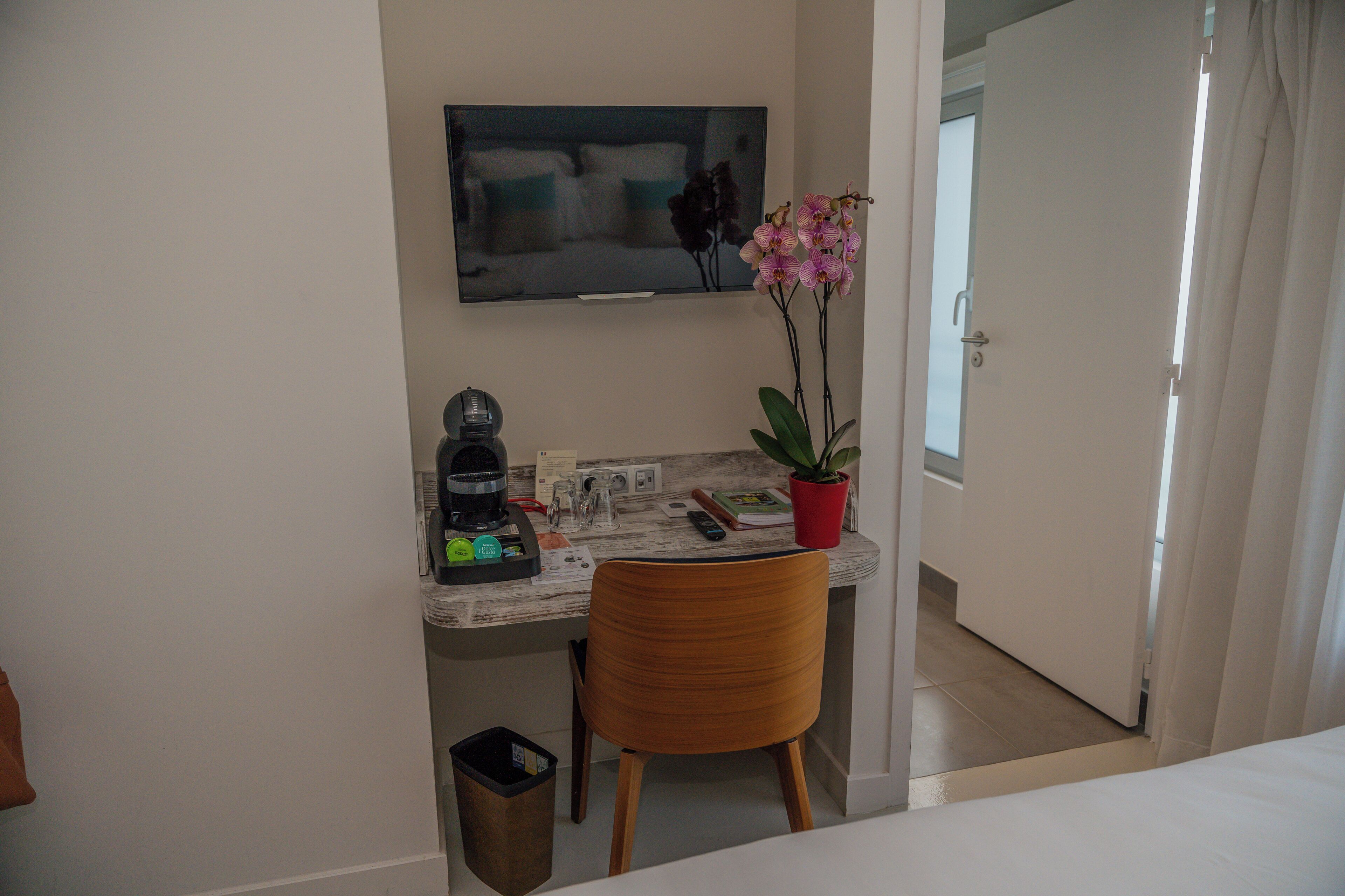 Habitació d'hotel petita amb escriptori, televisió, cadira, orquídia en test i safata de brossa.