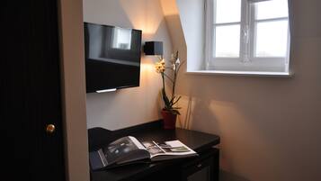 A room with a flat-screen TV mounted on the wall, a small potted plant, and a magazine on a desk.