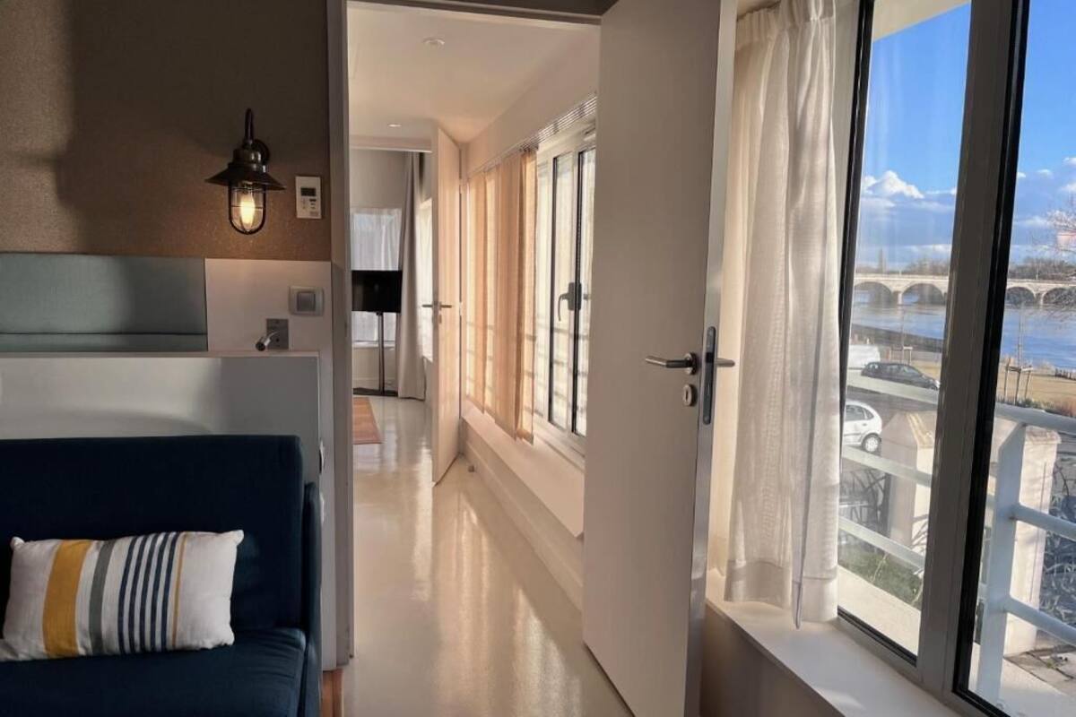 Una habitación de hotel moderna con un ventanal grande, un sofá y un pasillo que lleva a un baño.