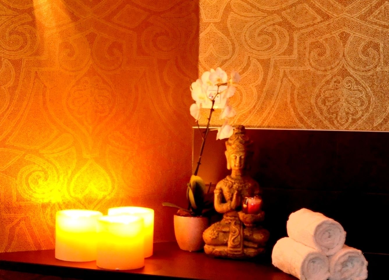 Ein Zimmer mit Buddha-Statue, einer Topfpflanze und eingerollten Handtüchern auf einem Regal.