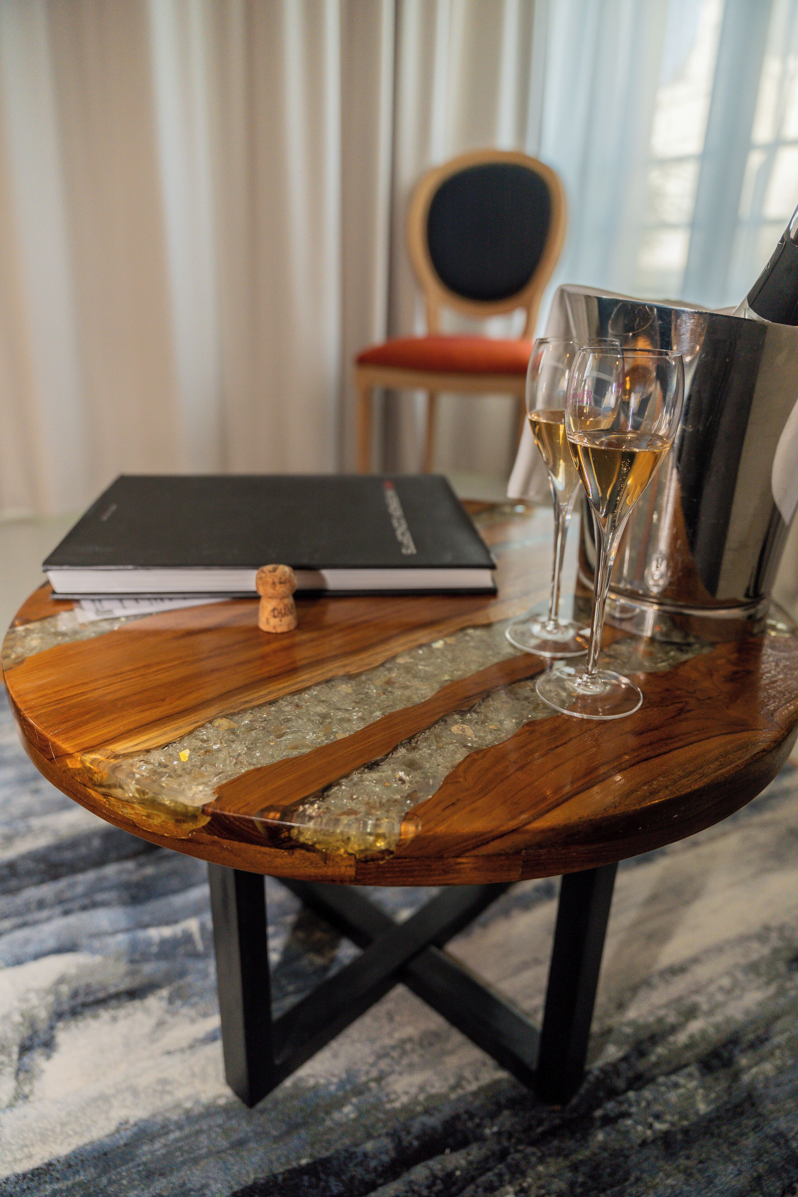 A wooden table with a glass of champagne, a cork, and a book.