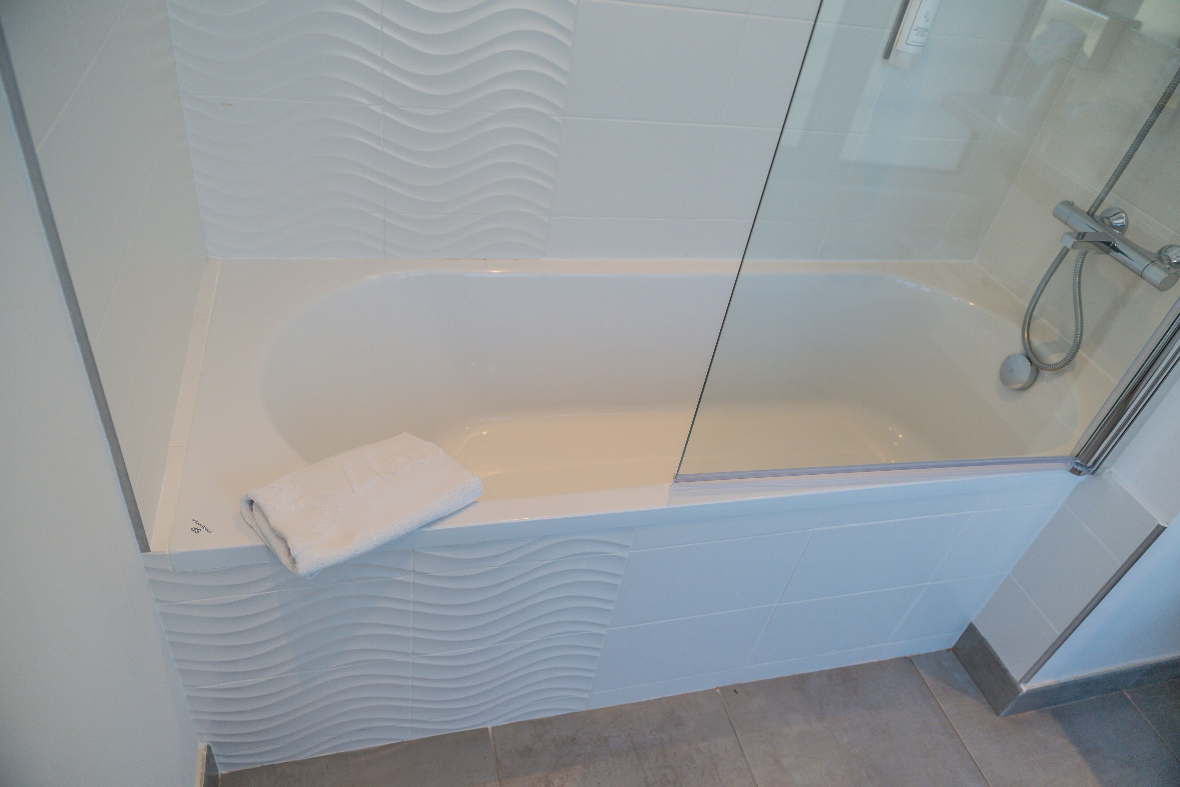 Un baño moderno con una bañera independiente, una cabina de ducha de vidrio y una toalla blanca sobre la bañera.