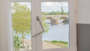 Vista a través de una ventana: un río con un puente de piedra, vegetación y cielo despejado.