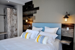 A neatly made bed with white linens and striped pillows, a blue headboard, and wooden wall decor. - Les 3 Lieux - Hôtel, Restaurant, Espace sensoriel (Les Ponts-de-Ce)