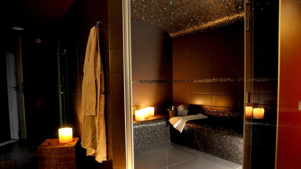 Un baño moderno con cabina de ducha de vidrio, un banco de madera y dos velas encendidas.