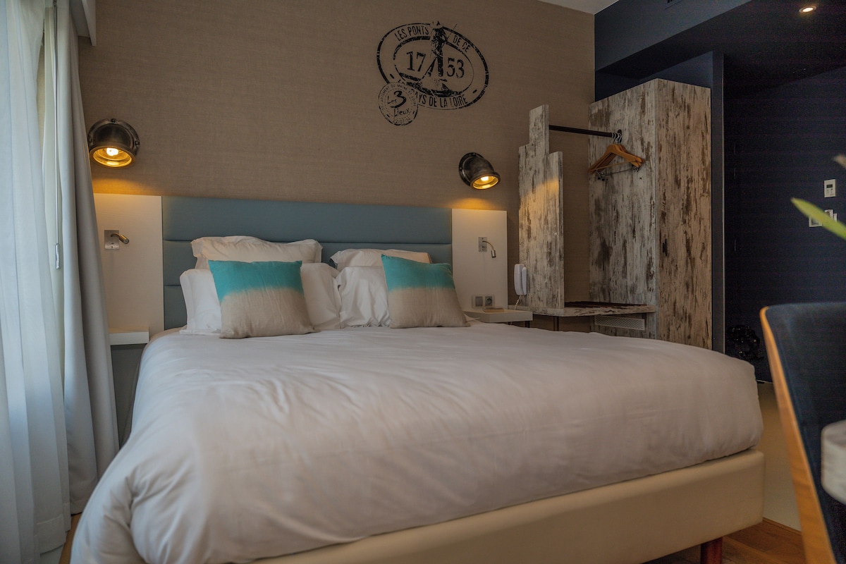 Una cama bien hecha con un cabecero azul, dos lámparas de noche y un reloj de pared.