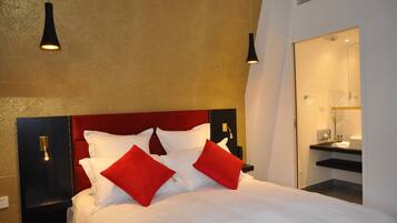 Ein Hotelzimmer mit einem Bett, roten und weißen Kissen, einem Nachttisch und zwei Pendelleuchten.