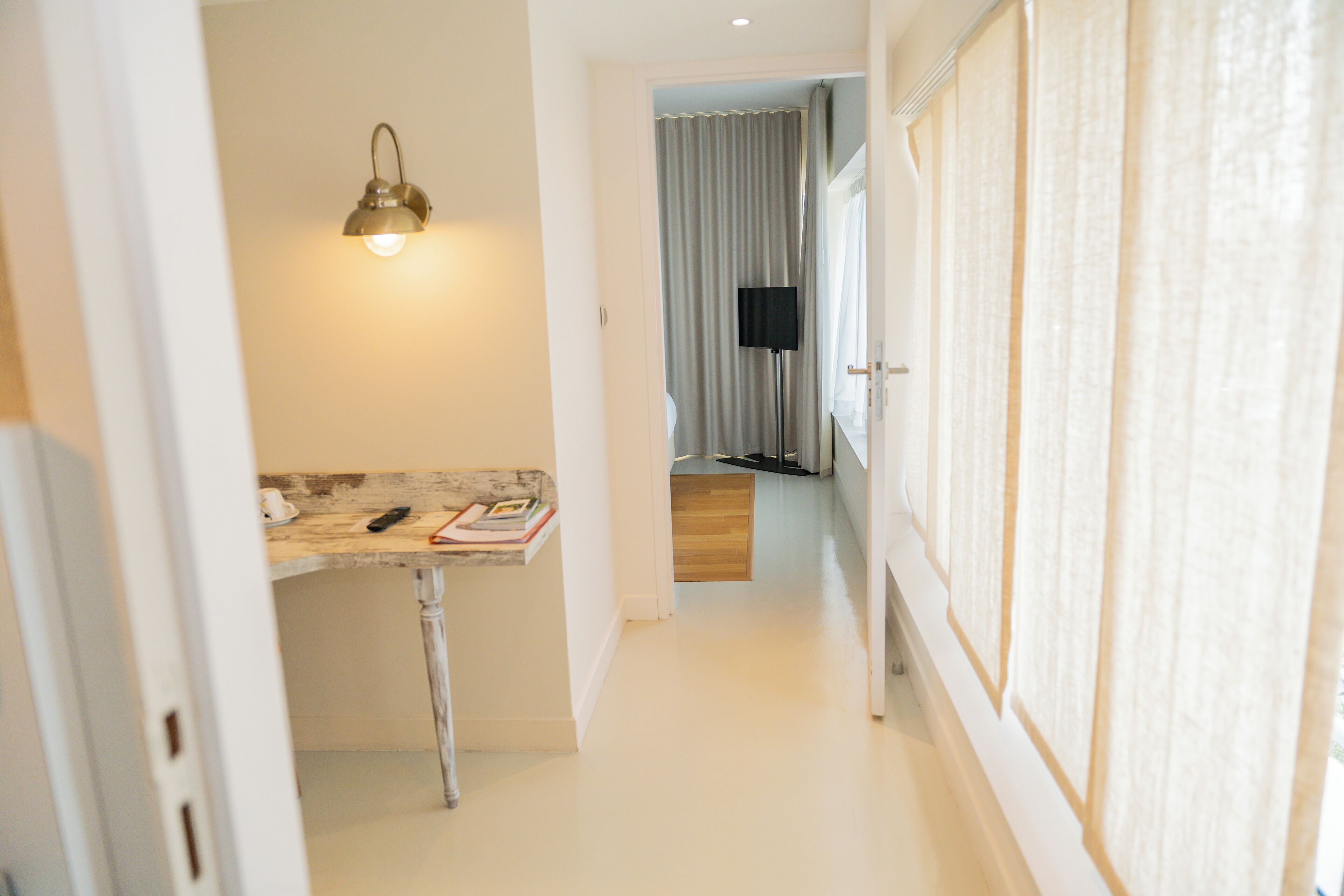 Un couloir avec un luminaire, un téléviseur à écran plat et une porte donnant sur une pièce séparée par un rideau.