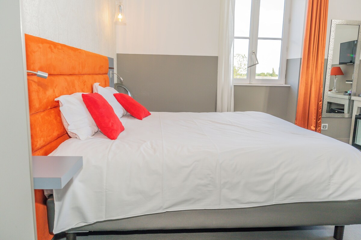 Habitación de hotel con cama, mesita de noche, espejo y ventana con cortinas.