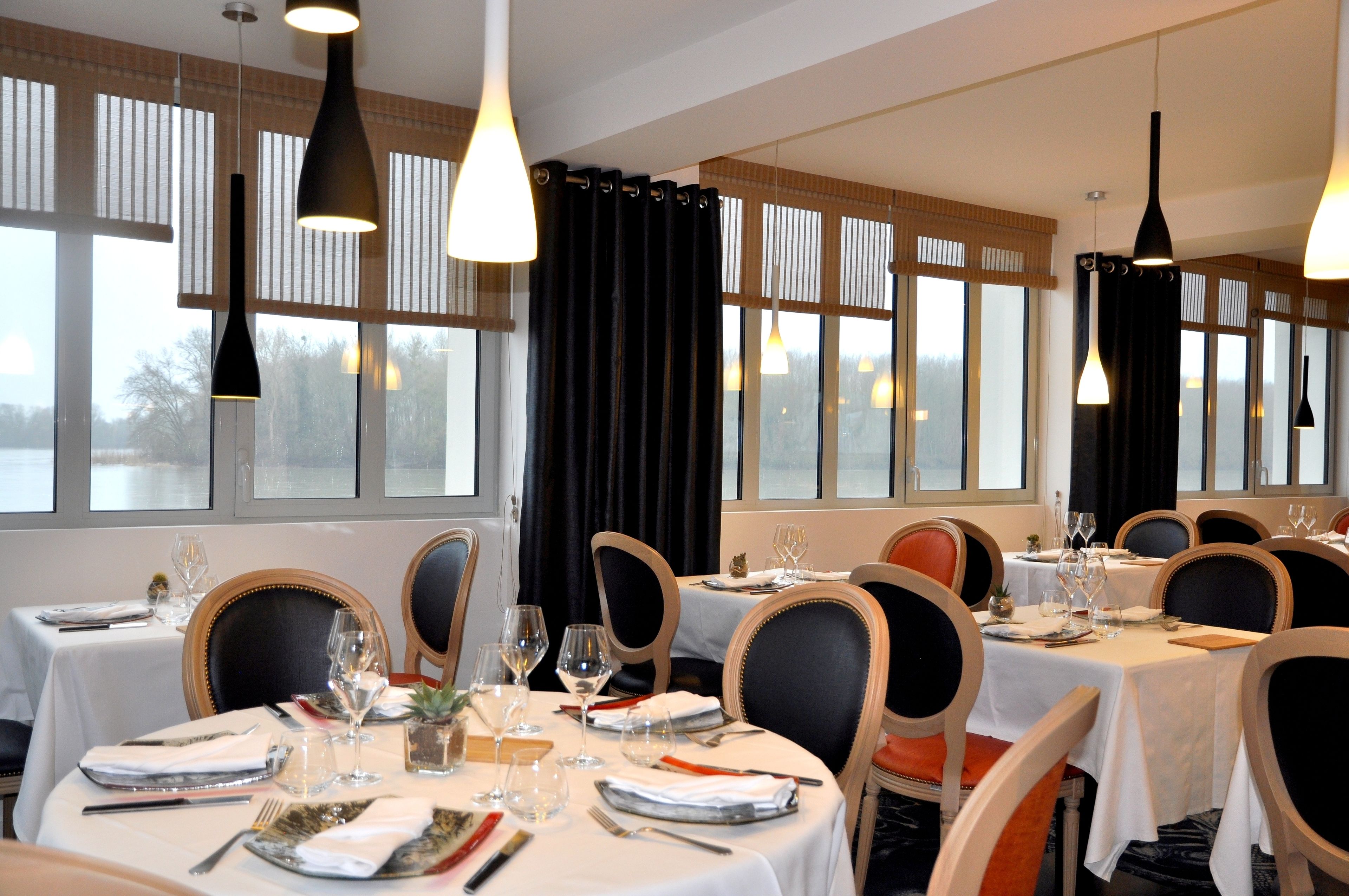 A dining area with tables set for four, each with white tablecloths, black chairs, and hanging pendant lights.