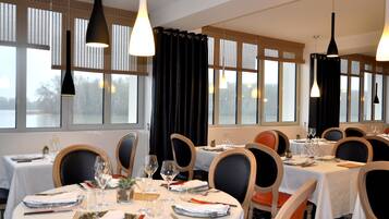 A dining area with tables set for four, each with white tablecloths, black chairs, and hanging pendant lights.