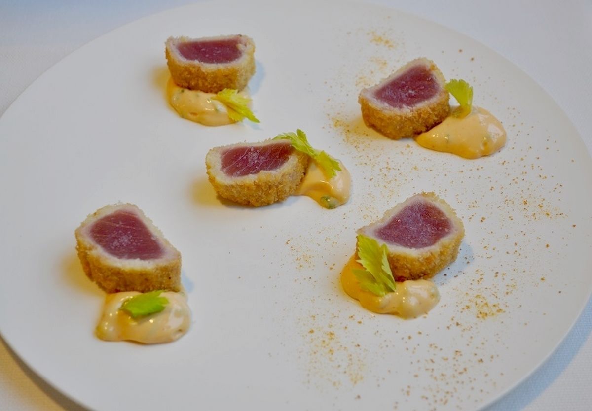 A plate with five pieces of food, each with a golden-brown crust and a pink center, accompanied by a yellow sauce and green garnish.