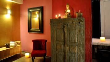 A room with a mirror, a red chair, a cabinet with a Buddha statue, and candles.