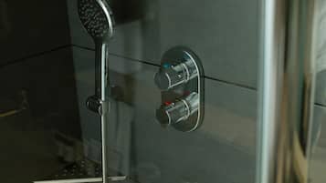 A shower with a handheld showerhead and a wall-mounted control panel with two knobs.