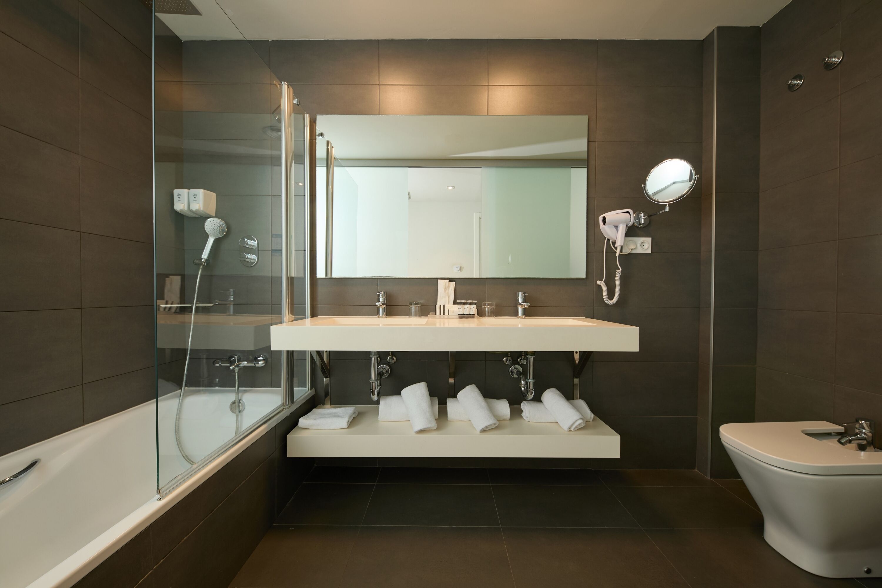 A modern bathroom with a glass-enclosed shower, a white sink with a mirror above, and a toilet.