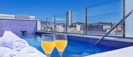 A rooftop pool with two glasses of orange juice and rolled towels.
