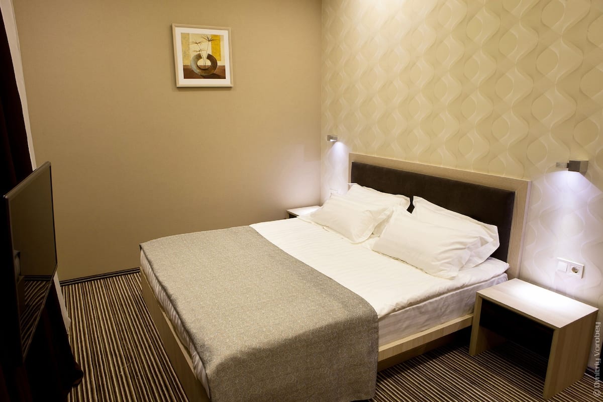 A hotel room with a bed, bedside table, and a wall-mounted lamp.