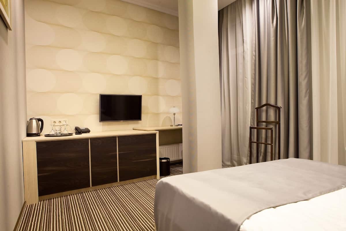 A hotel room with a bed, a TV mounted on the wall, a minibar, and a window with curtains.