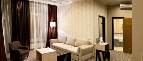 A hotel room with a sofa, armchair, small table, and a mirror.