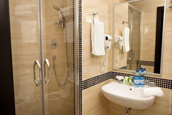 Une salle de bain avec une douche à parois de verre, un lavabo blanc et un miroir auquel est accrochée une serviette au mur.