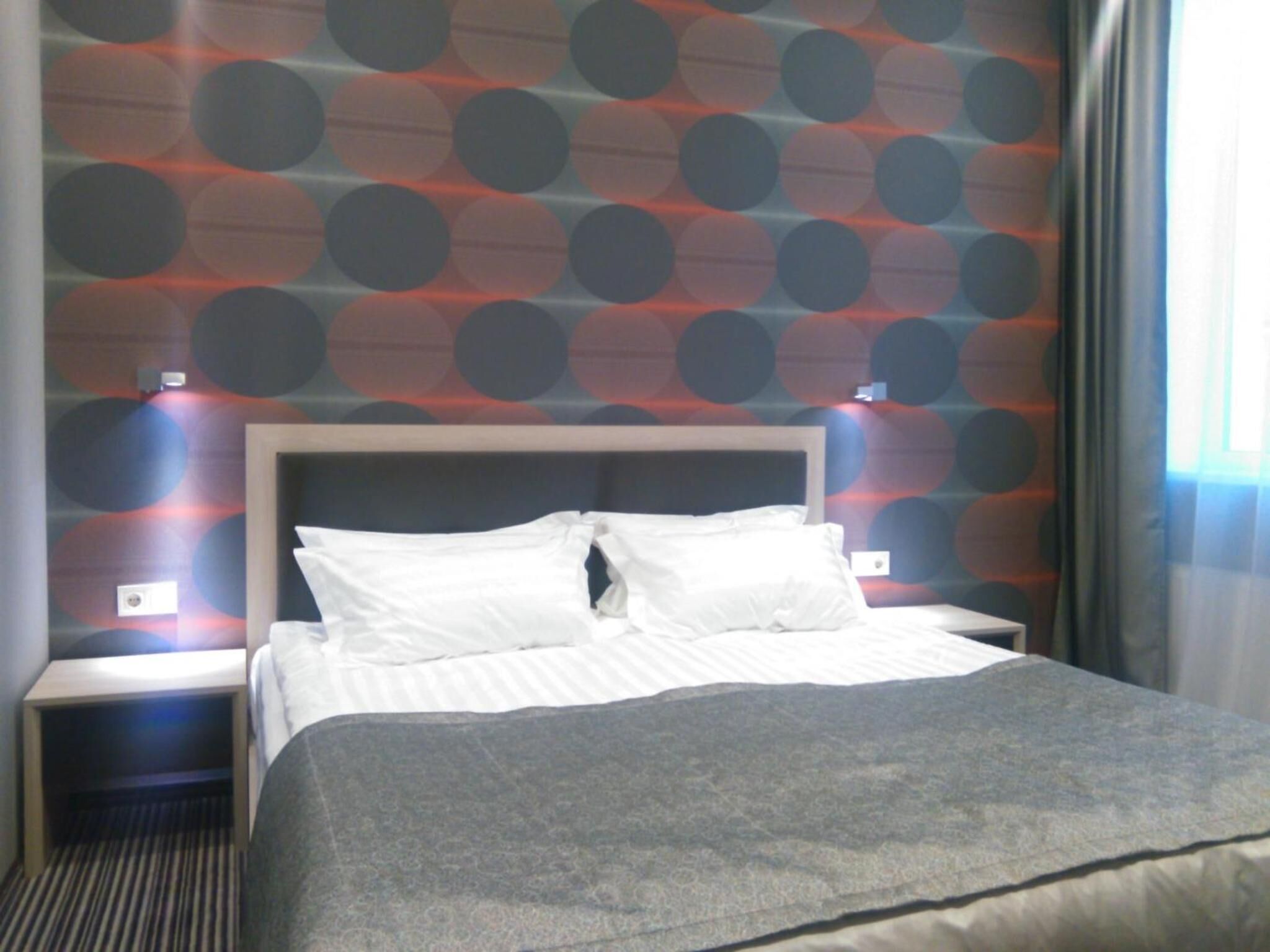 Habitación de hotel con una cama, dos mesitas de noche, un cabecero y un papel tapiz estampado.