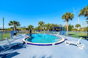 Una piscina con azulejos azules, rodeada de palmeras y una valla azul.