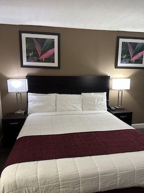A hotel room with a large bed, two bedside tables with lamps, a dark headboard, and two framed pictures on the wall. - Rodeway Inn Bushnell (Bushnell)