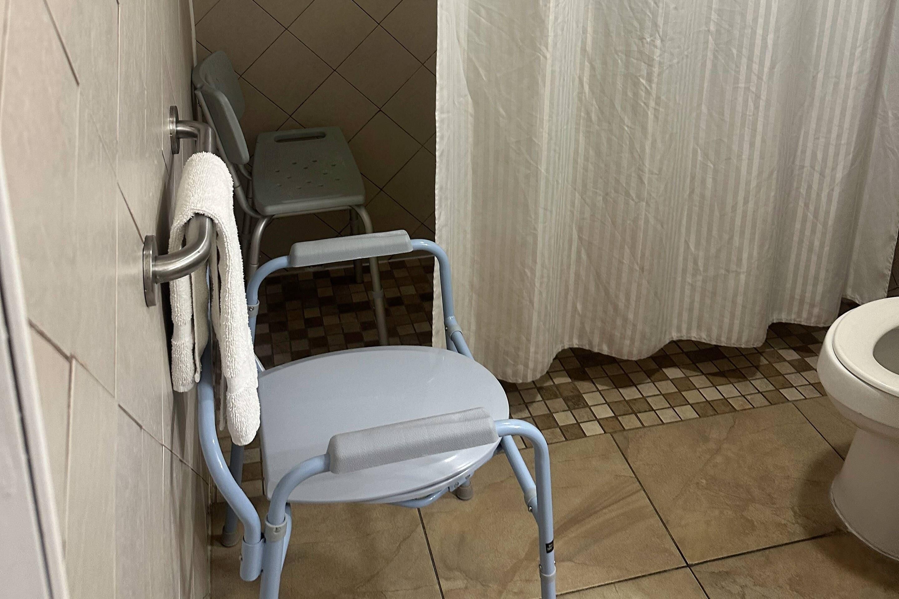 Un baño con silla de ruedas, una mesita pequeña y un inodoro.