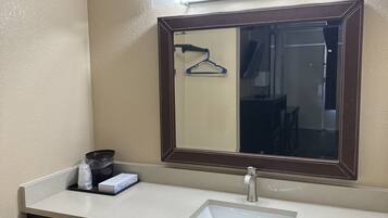 A bathroom with a white sink, a mirror with lights, a towel rack, and a trash bin.