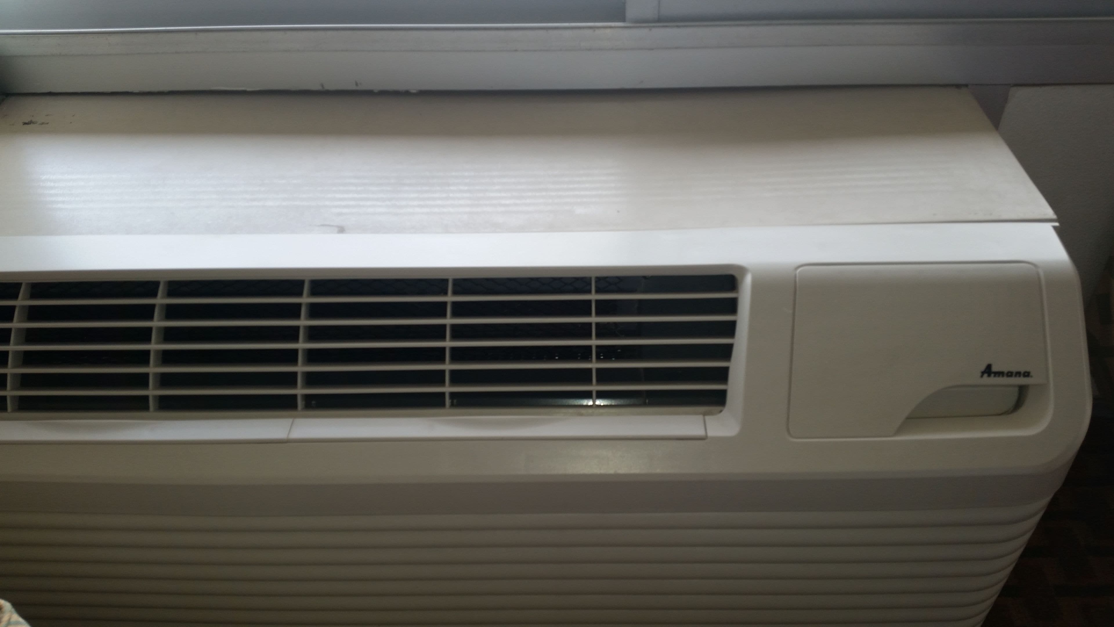 Un equipo de aire acondicionado blanco con una rejilla y un panel de control etiquetado como 'Amana'.