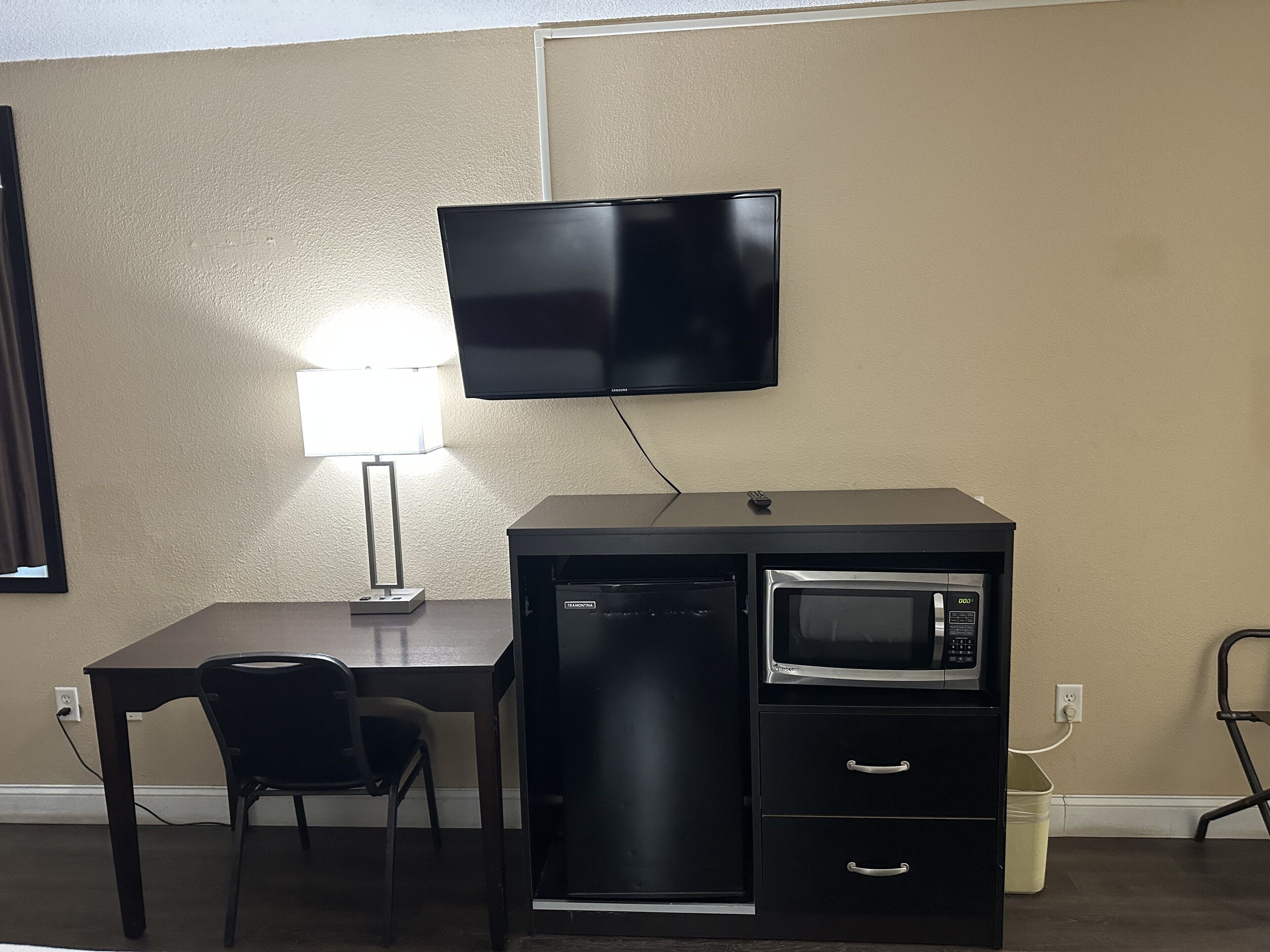 Une petite cuisine équipée comprenant un four à micro-ondes, un petit réfrigérateur, un bureau avec une chaise et un téléviseur fixé au mur.