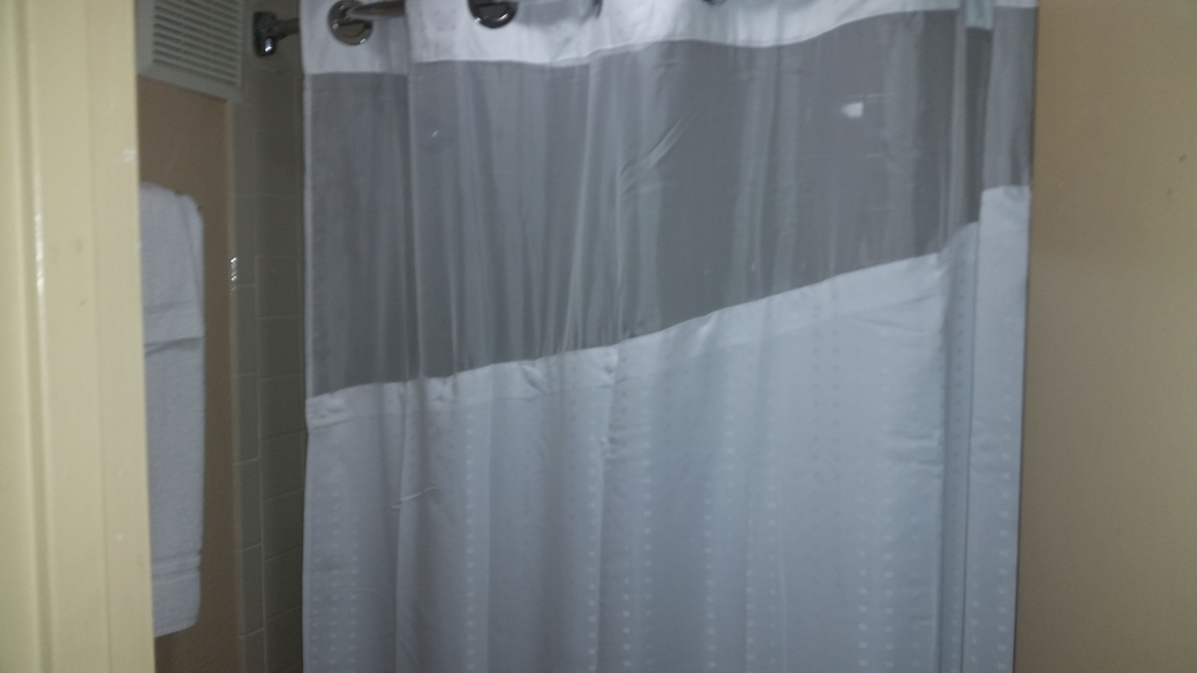 A bathroom with a shower curtain, a towel rack, and a tiled wall.