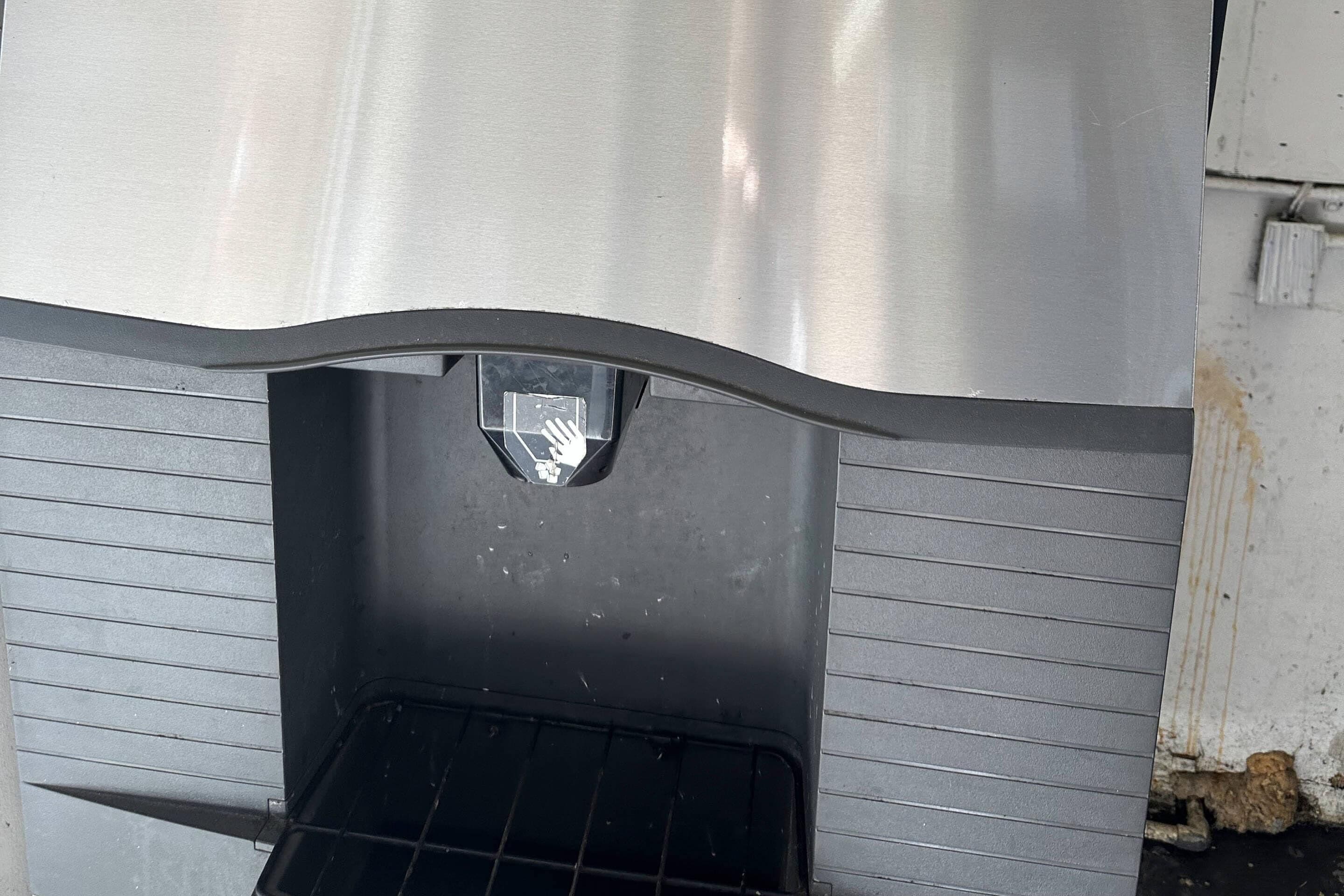 A metallic, curved structure with a rectangular opening, possibly a vent or access point, and a black grid-like base.
