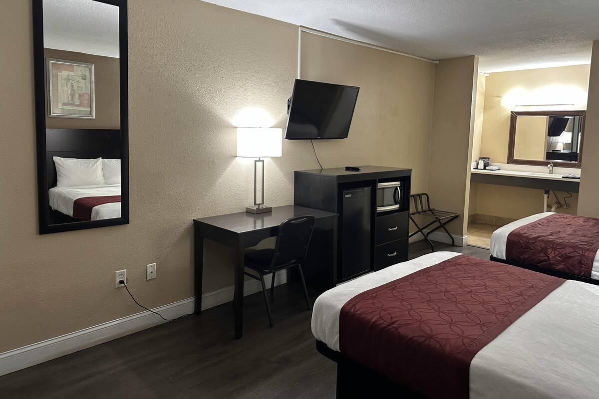 A hotel room with two beds, a desk, a chair, a TV, and a mirror.