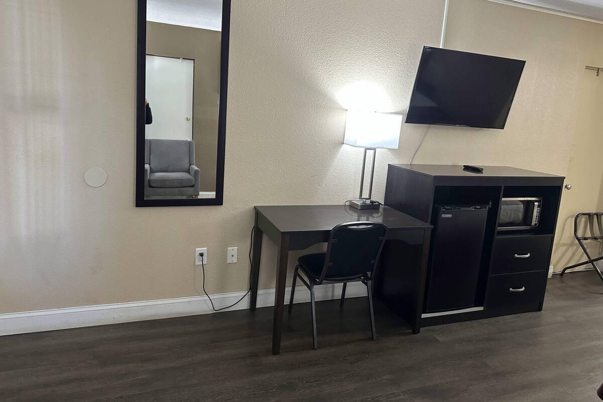A hotel room with a desk, chair, TV, and a minibar.