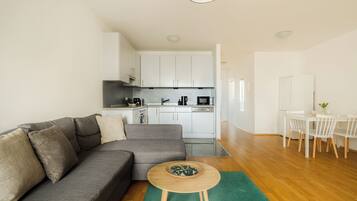 A modern living room with a grey sofa, a small wooden table, and a dining area with a white table and chairs.