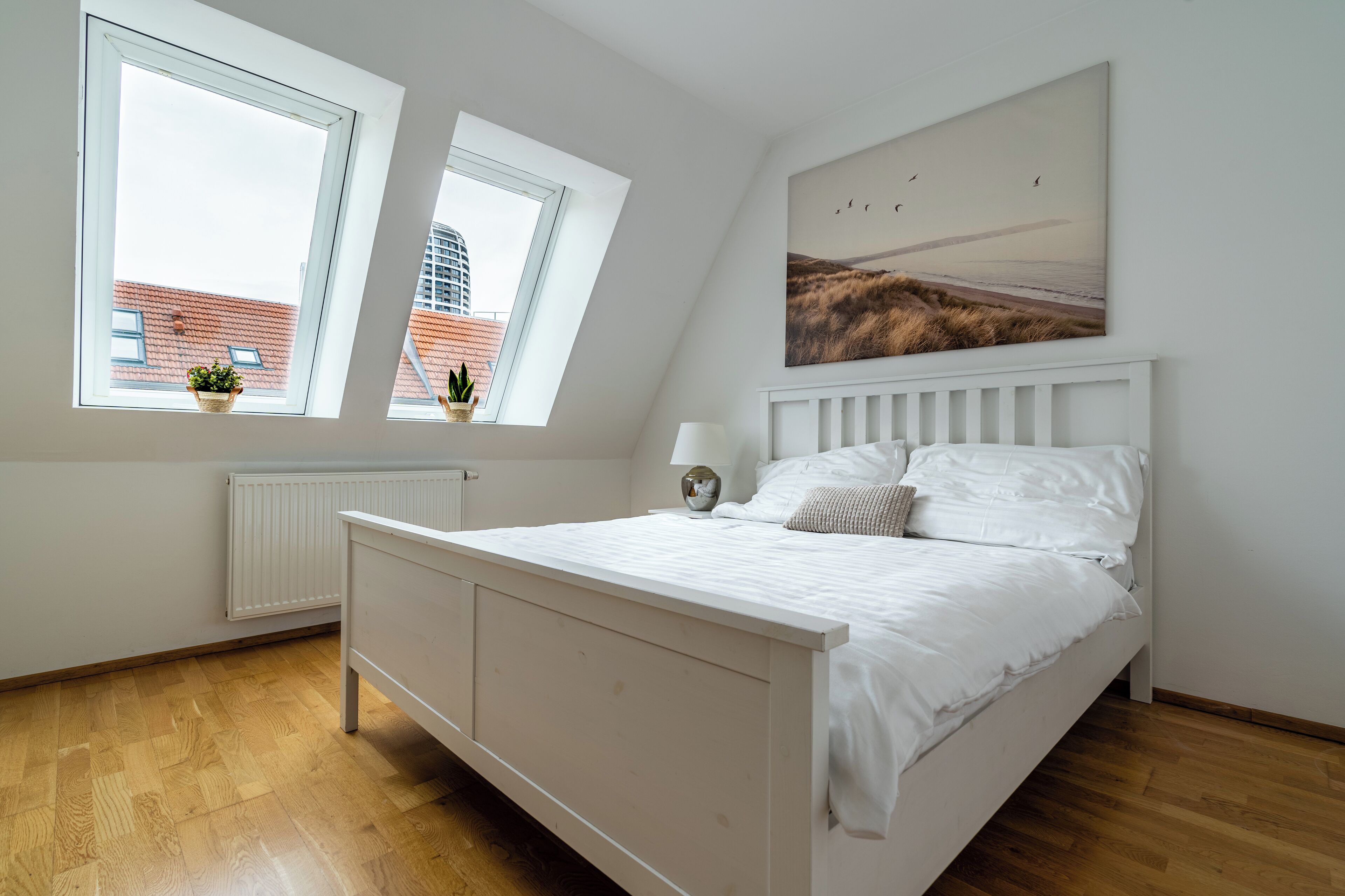 A bedroom with a bed, two windows, a radiator, and a painting on the wall.