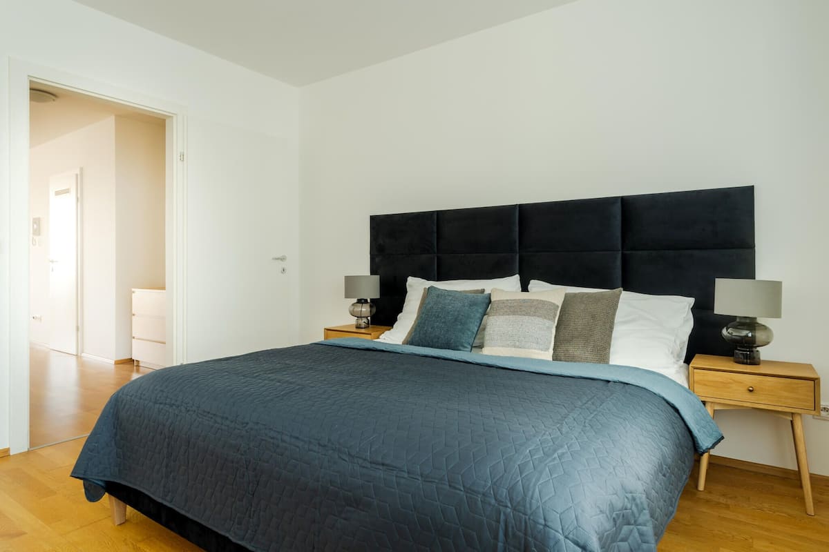 A bedroom with a large bed, a dark headboard, two bedside tables with lamps, and a wooden floor.