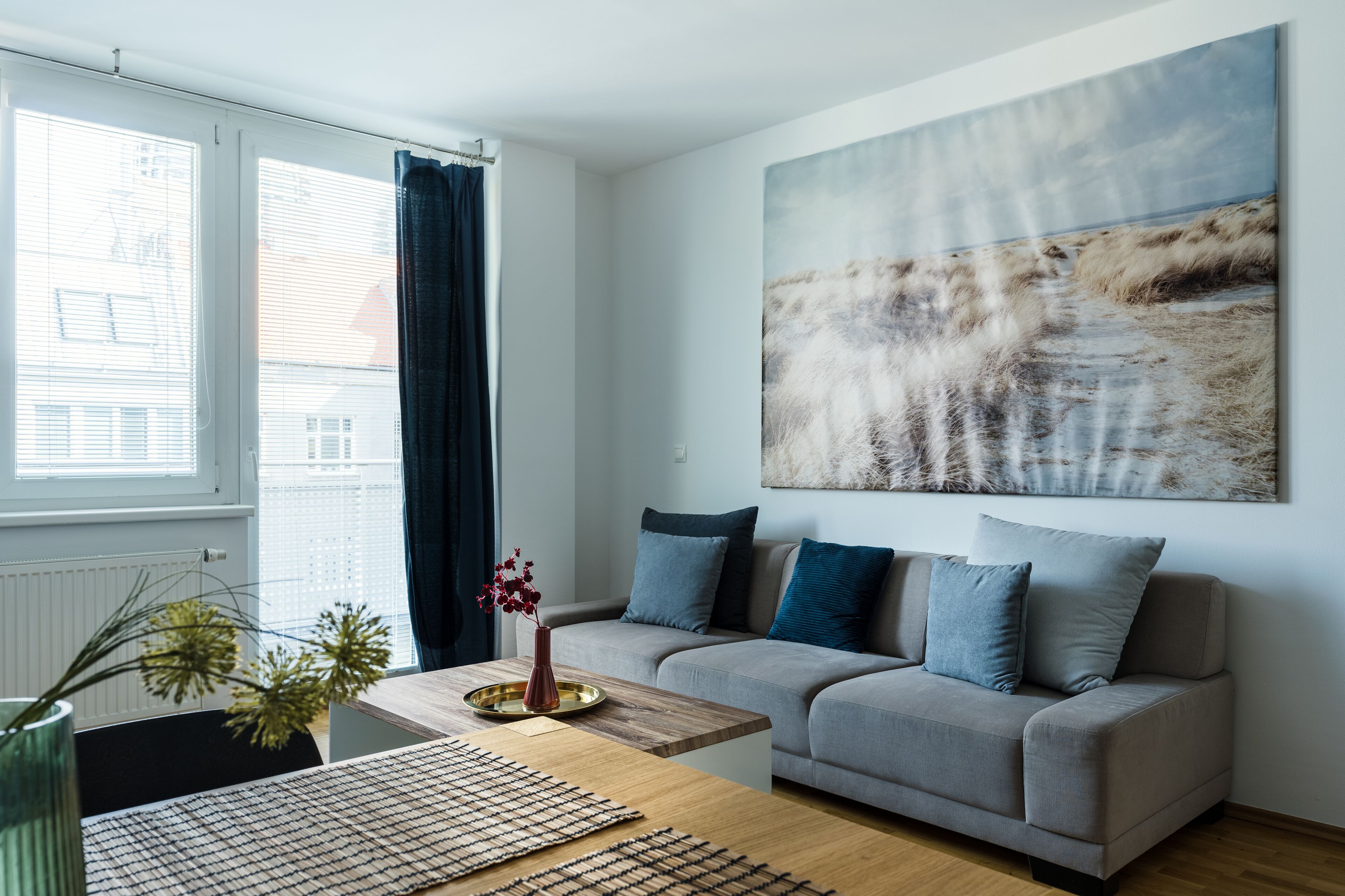 Uma sala de estar moderna com um sofá cinza, uma mesa de centro de madeira e um grande quadro abstrato na parede.