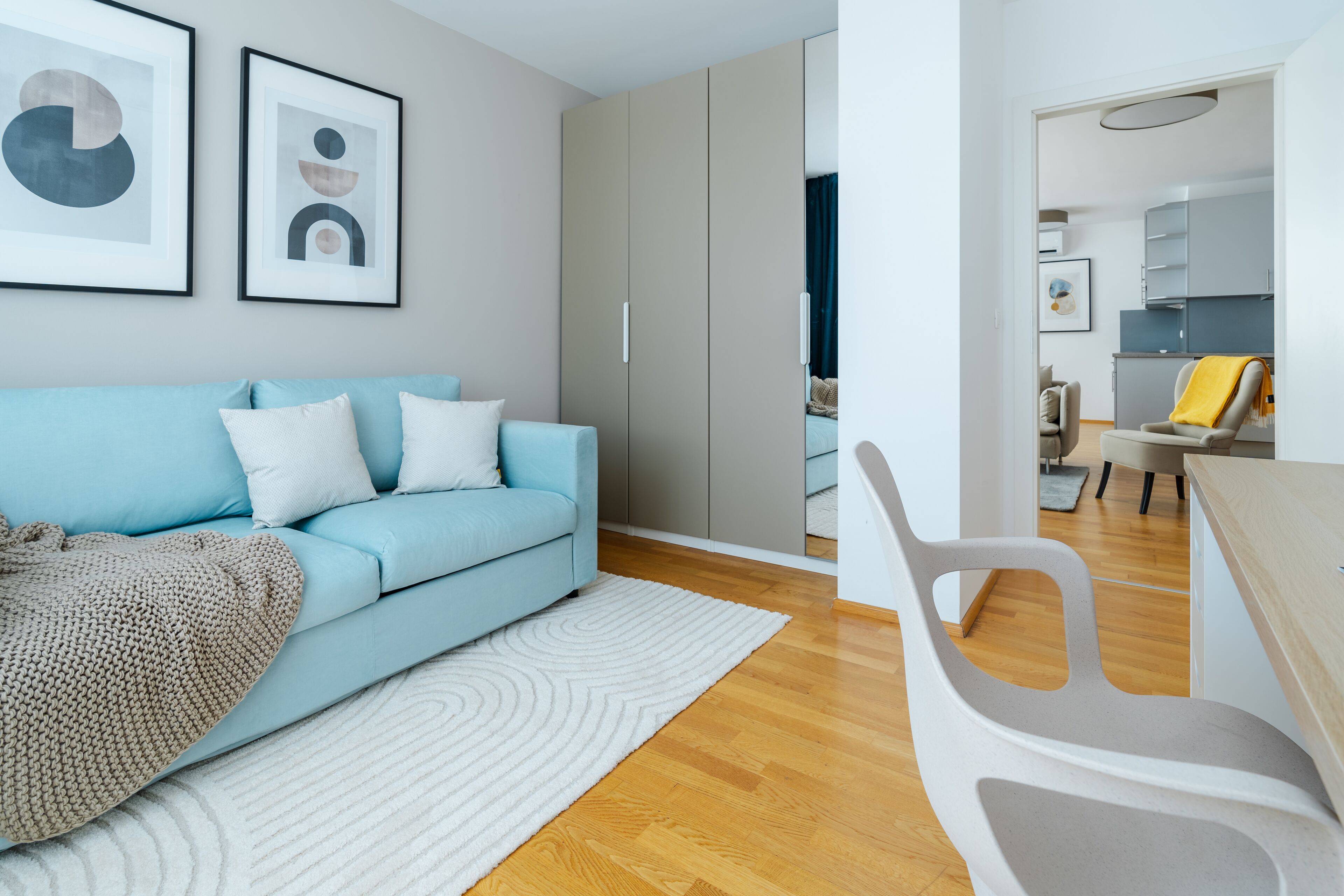 A modern living room with a light blue sofa, white cushions, a white rug, and a grey chair.