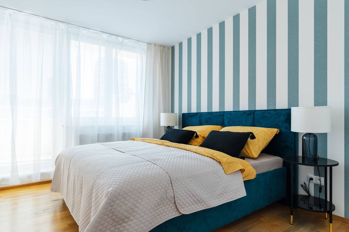 A modern bedroom with a teal upholstered bed, white bedding, and a yellow throw blanket.