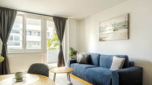 A modern living room with a blue sofa, a small round table with two cups, and a view of the outside through large windows. - Business & Family Ambiente Apartments (Bratislava)