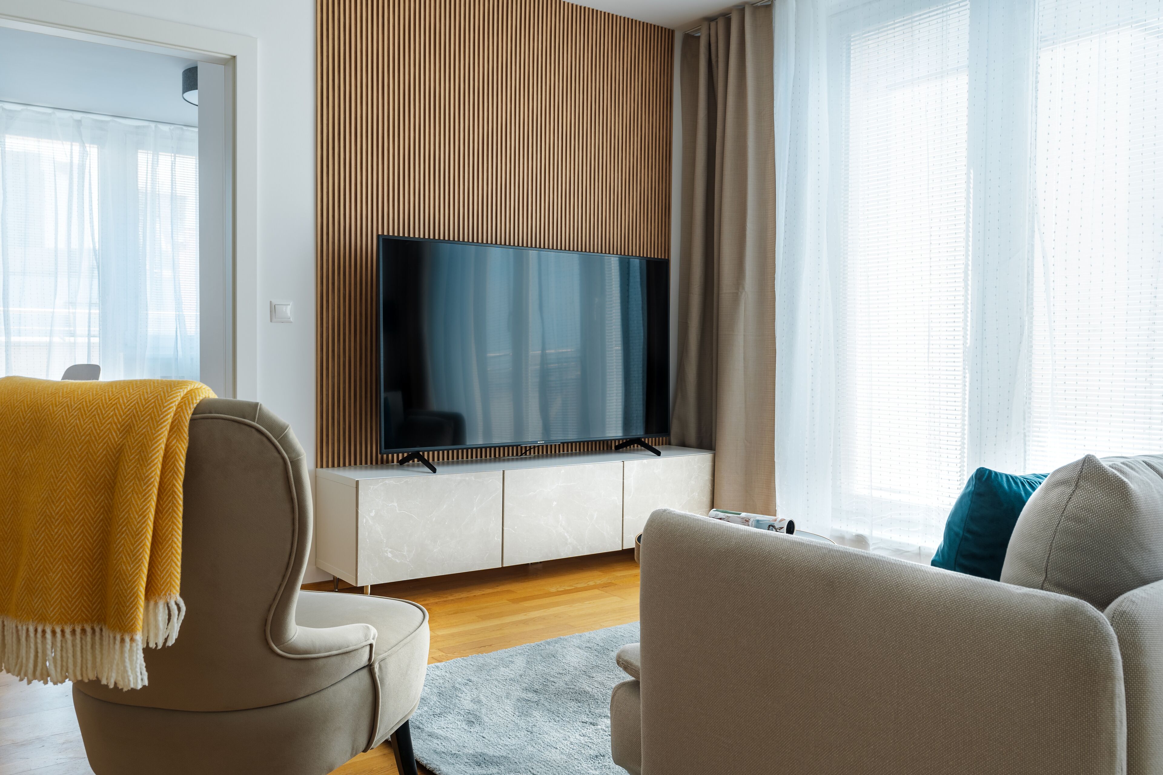 Un salon moderne avec un canapé, un fauteuil et un téléviseur à écran plat fixé au mur.