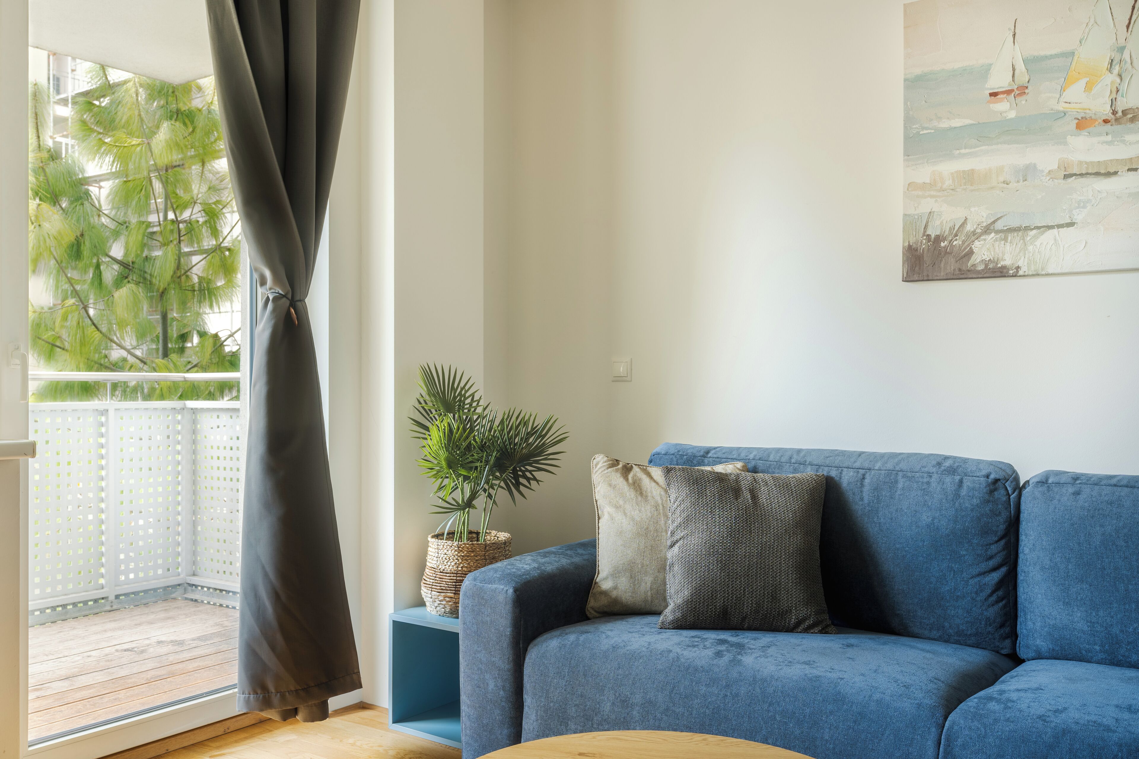 Een woonkamer met een blauwe bank, een potplant en een schilderij aan de muur.